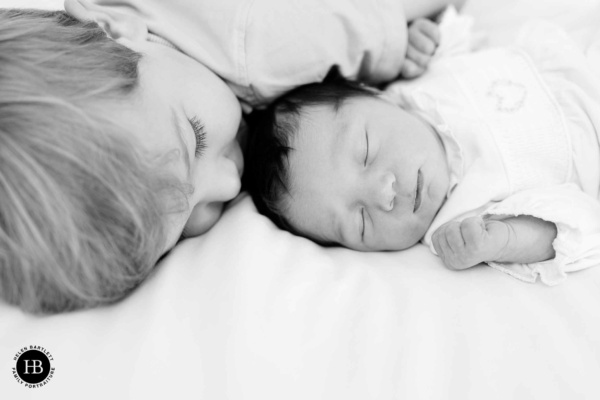 newborn baby sleeps while older brother kisses her head during professional newborn baby photo shoot in Hampstead NW3 and NW5