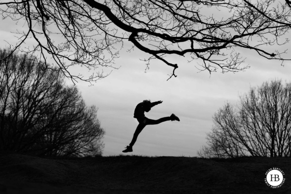 A girl dances on the horizon, framed by tree silhouettes in this evocative black and white photo taken during a portrait session in London.