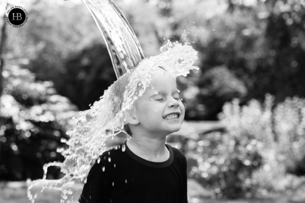 A black and white photo of a girl having water dumped on her head amidst huge giggles.