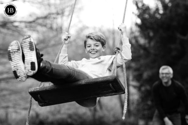 Black and white family photography of a boy on a swing.