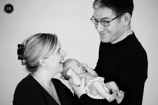 Two parents in dark clothing holding their newborn at home — a simple, timeless choice for black and white photography
