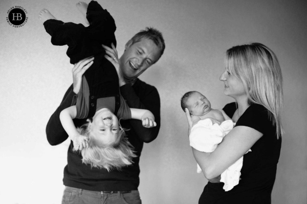 Parents playing with their toddler while cradling their newborn — a candid black and white family moment at home