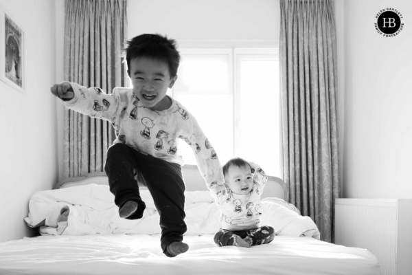 Toddler jumps on the bed while baby brother looks on