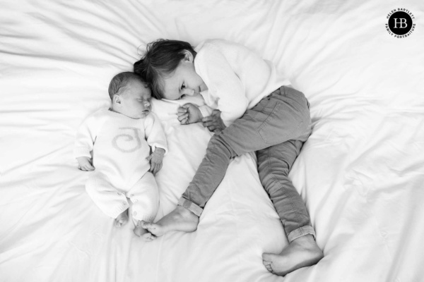 Big brother touches his newborn baby siblings toes while lying on their parents bed