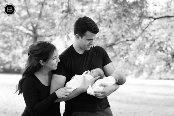 Dad holds newborn twins while mum looks on during a socially distanced outdoor newborn photography session