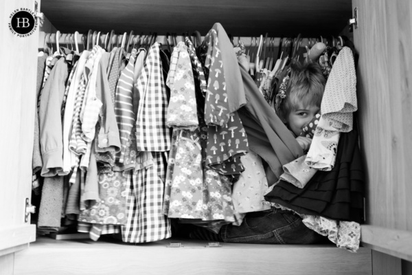 boy hides in a wardrobe during a game of hide and seek. Image used to illustrate what to wear on a family photo shoot