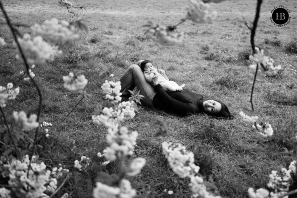 mother-and-baby-lie-on-grass-framed-by-blossom-battersea-park-london