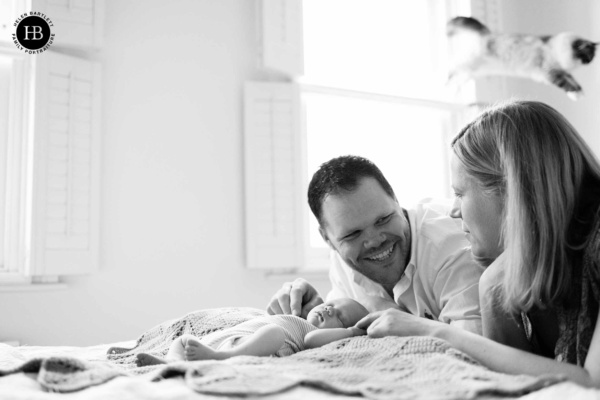 mum-and-dad-smile-with-newborn-baby-while-cat-jumps-over-mums-head
