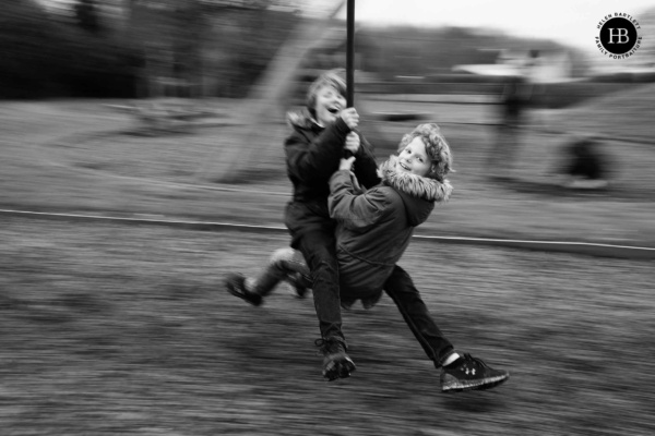 Two children speed by on a zip line in this happy sibling photograph. Taken using the panning technique to show the speed by photographer Helen Bartlett.