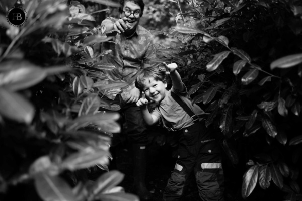 father and son run through the undergrowth laughing and pointing to the camera - they have found the photographer during a game of Hide and Seek