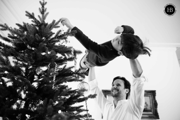 A father lifts his son to decorate the tree on a Christmas themed family photo shoot