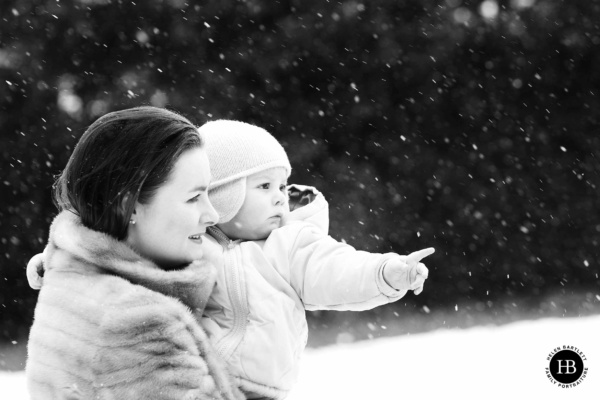 A snowy family photo with glamorous mother holding her baby in a beautiful notting hill square covered in a blanket of snow