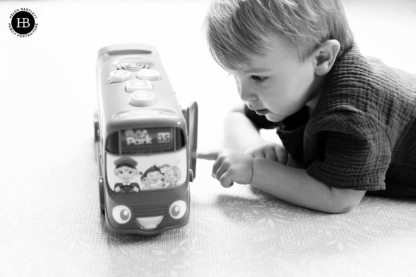 Little boy lies on the floor playing with a toy bus during an at home family photography session.