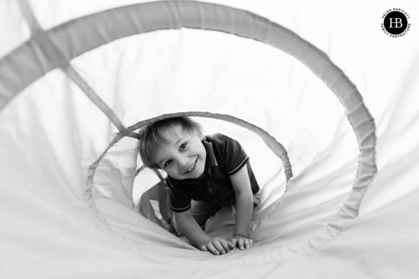 Little boy looks through a play tunnel laughing on an at home family photography session.