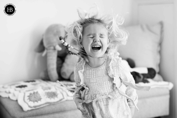 Little girl jumps for joy in her childhood bedroom. Her hair and necklace are flying as she screams in delight