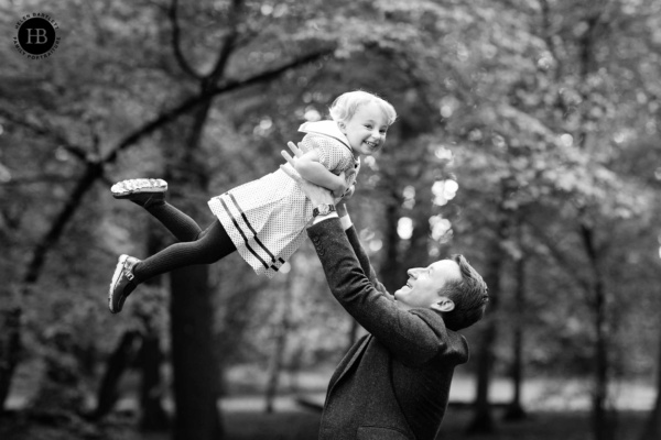 Father throws daughter in the air in a stunning woodland setting. Both are laughing in delight