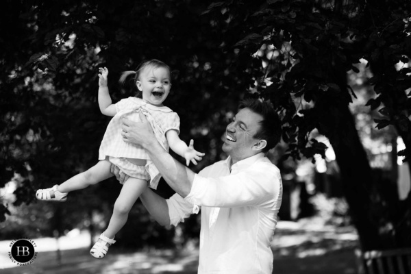 Father and daughter play in the woods on a sunny day. He is holding her in the air and they are boy laughing in delight.