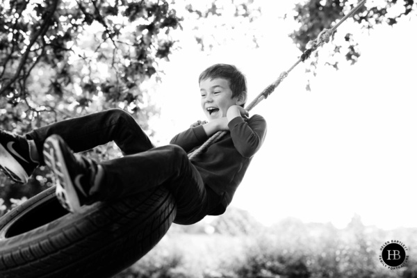 young boy swings close to the camera lens on a tyre swing attached to a tree in a glorious at home summer family photo