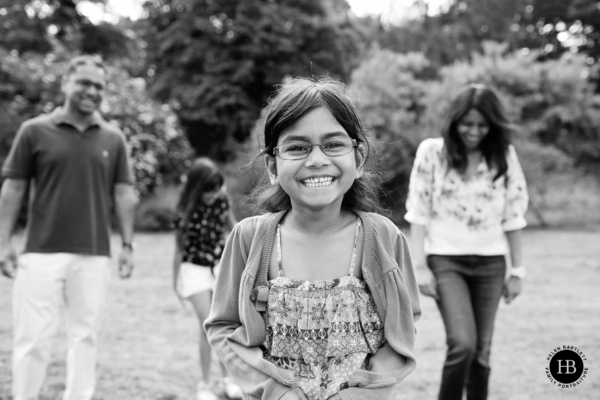 girl laughs with her family in the background during a game of What's the time Mr Wolf on an outdoor family photo shoot in London in the summer