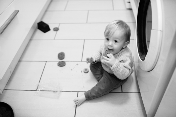 A baby sits on the floor, eating biscuits.