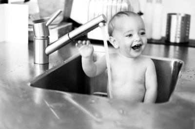 A baby bathes in a stainless steel sink.