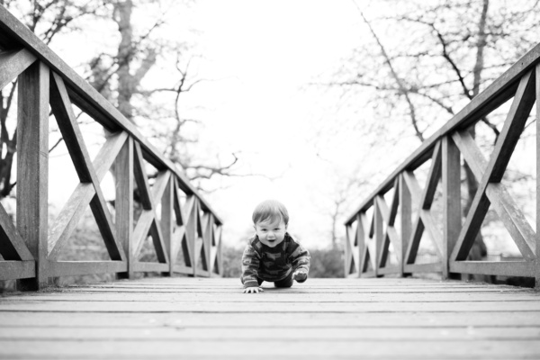 A baby crawls across a wooden bridge.