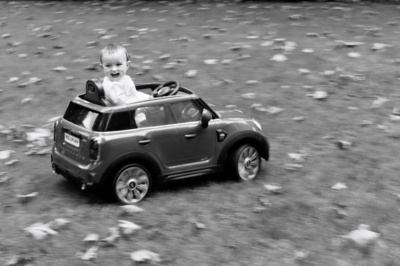 A baby drives a toy car across a lawn.