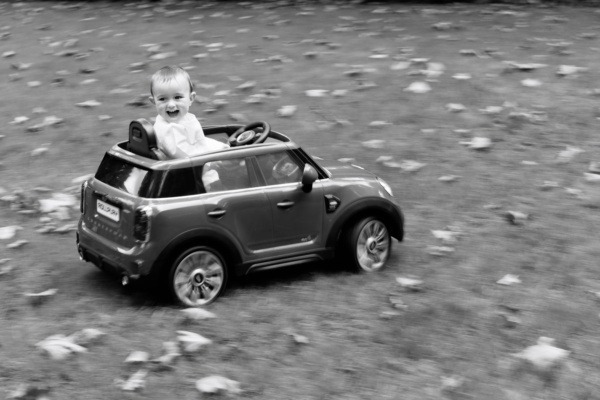 A baby drives a toy car across a lawn.