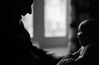 A baby and father smile at each other with a window in the background.