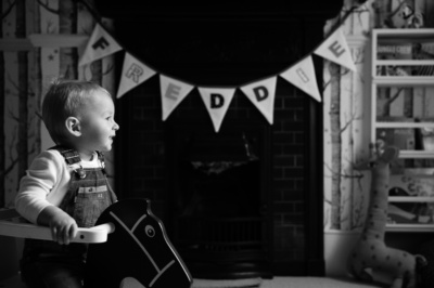 A baby in dungarees sits in a high chair.