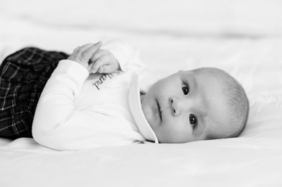 Baby lies on a bed, looking at the camera.