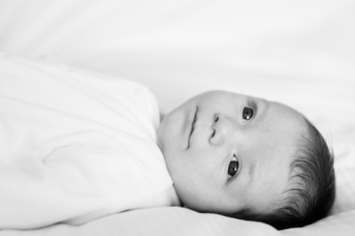 Baby lies on a white covered bed.