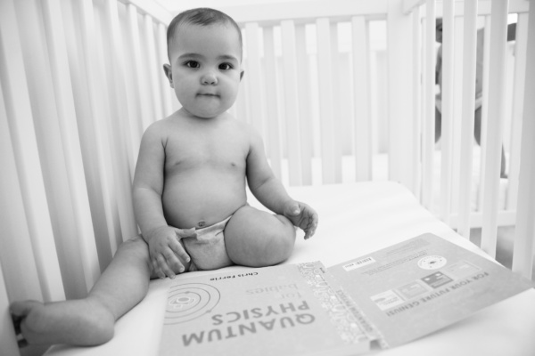 A baby looks at a book on quantum physics in their cot.