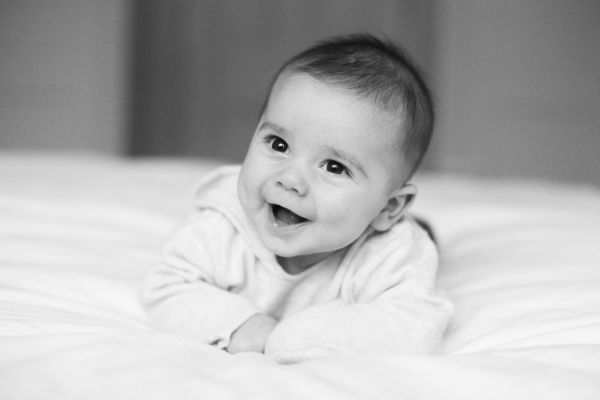 A baby on a bed smiles towards the window.