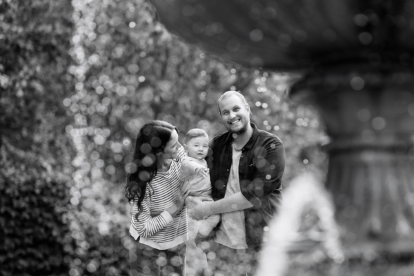 A portrait with a baby and their parents near a fountain.