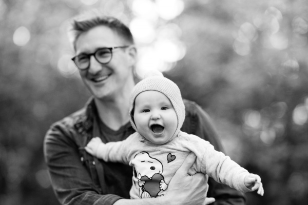 A baby sits on its father's lap in a park.