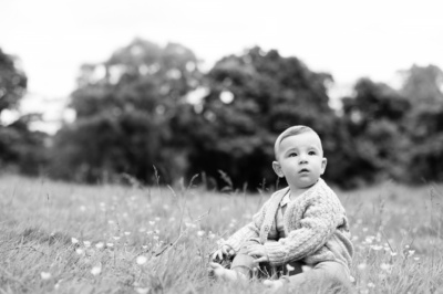 A baby sits in a field in a black and white portrait.