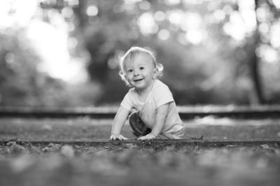 A baby sits in a park, smiling towards the camera.