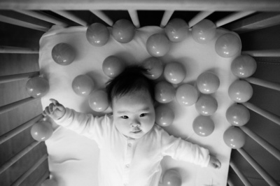 A baby plays with round toys in its cot.