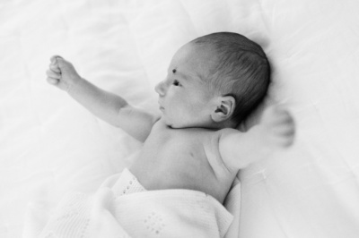 A baby waves their arms on their parents' bed.