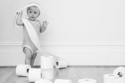 A baby wraps themselves in toilet roll.