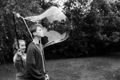 Boy blows giant bubble in a garden.