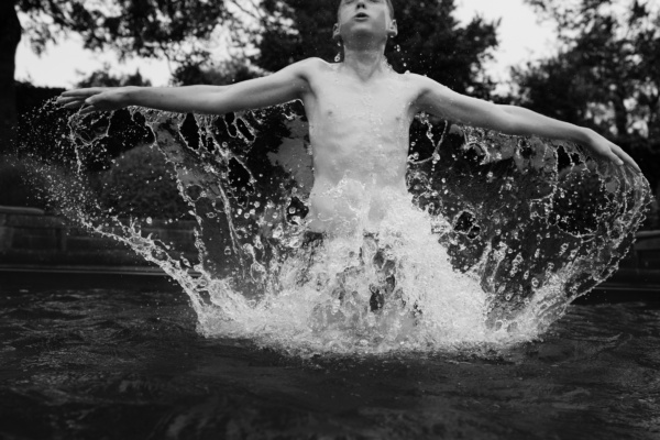 Boy emerges from the water with water dripping from his arms.