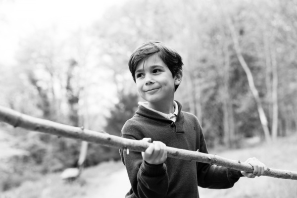 A boy plays with a tree branch.