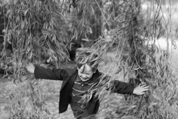 A boy runs through willow branches.