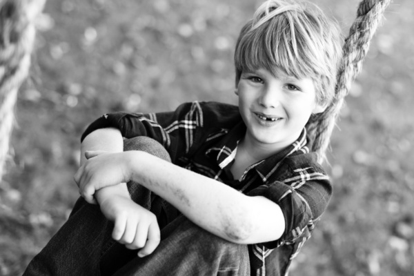 Boy sits on rope and wooden swing.