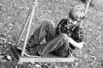 Boy sits on wood and rope swing.