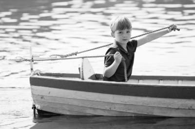 Boy skippers wooden dinghy across water.