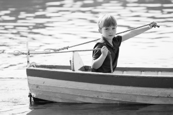 Boy skippers wooden dinghy across water.