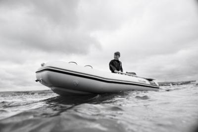 A boy skippers a rubber dinghy across the sea in Cornwall.